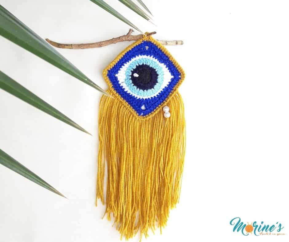 This free pattern for a Crochet Evil Eye Wall Art is made from crochet square. Accented with gold yarn and pearl beads for a tear drop effect.